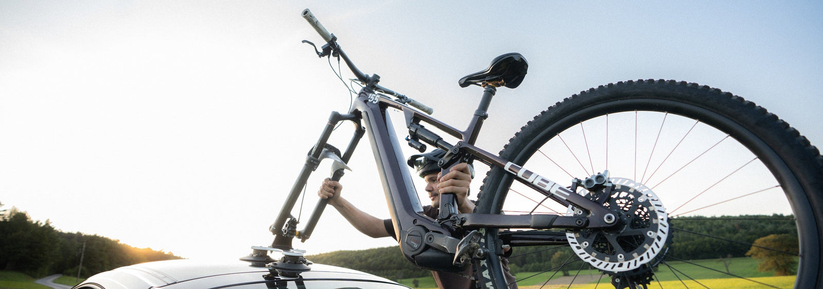 Person mounting a bicycle on a car roof with a scenic background